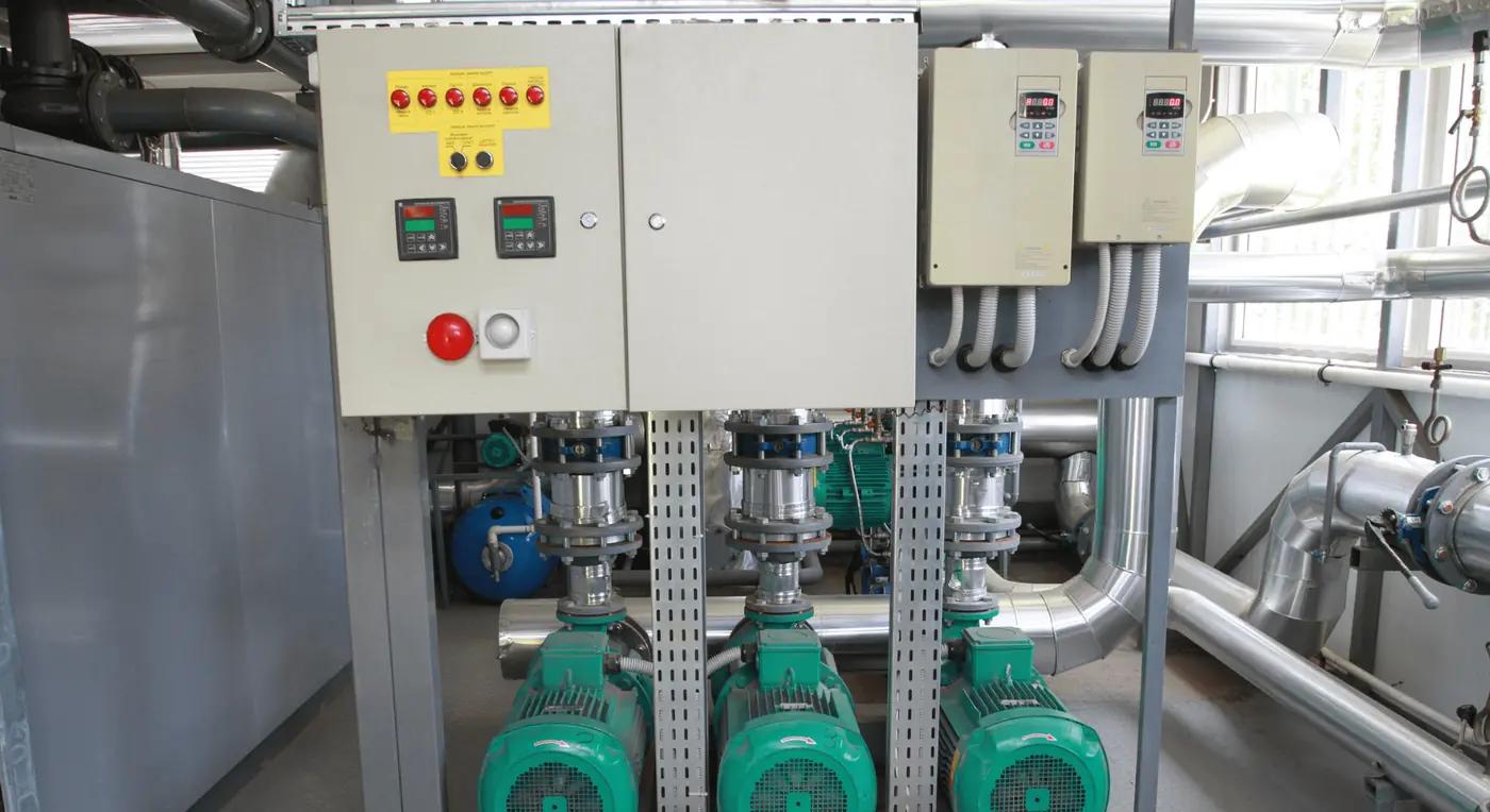A pump station interior: three vertical multistage pumps in line beneath their control panels, with valved discharge pipework above