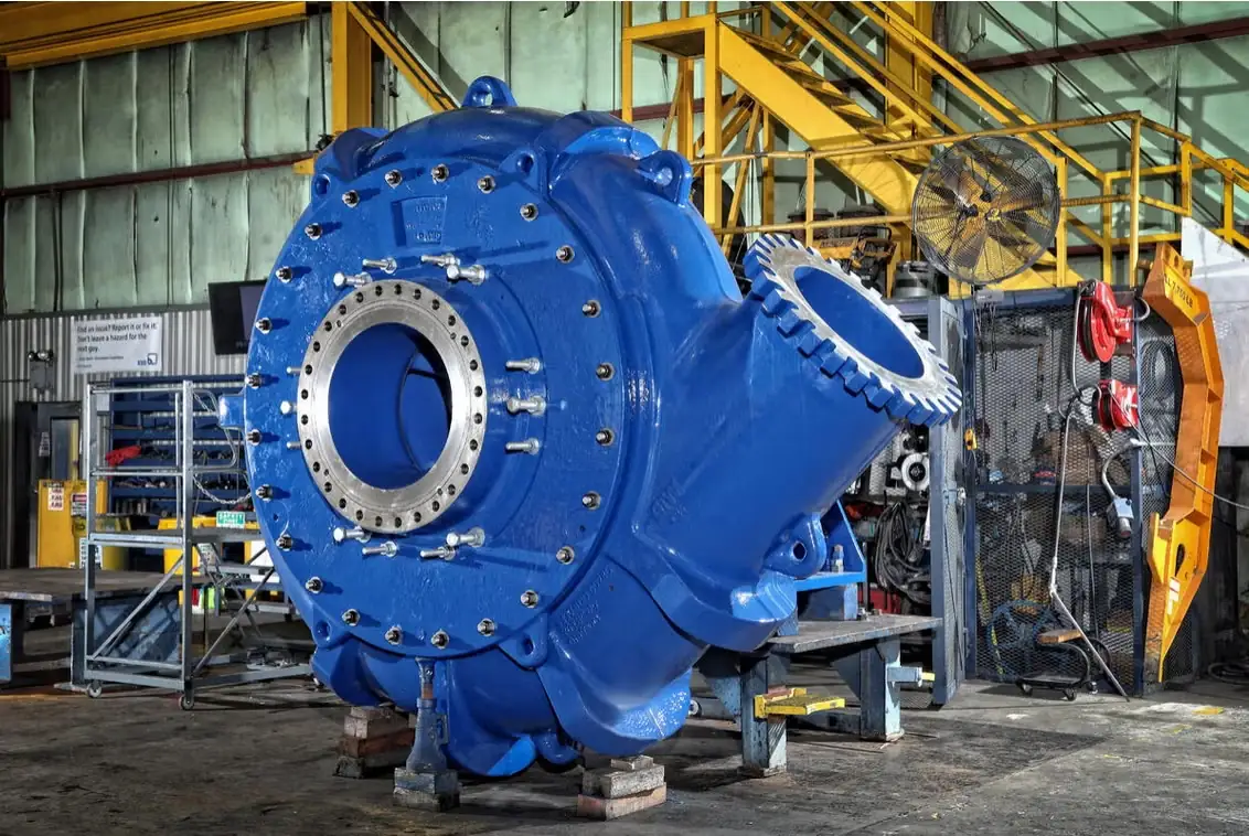 A large blue slurry pump casing on stands in the workshop, suction flange and drive end exposed
