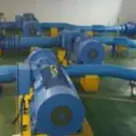 Blue pump sets and suction pipework mounted alongside a water channel at a treatment works